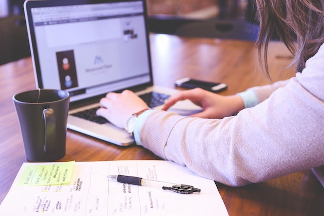 une personne travaillant avec un ordinateur portable, avec un carnet, un stylo et une tasse sur la table